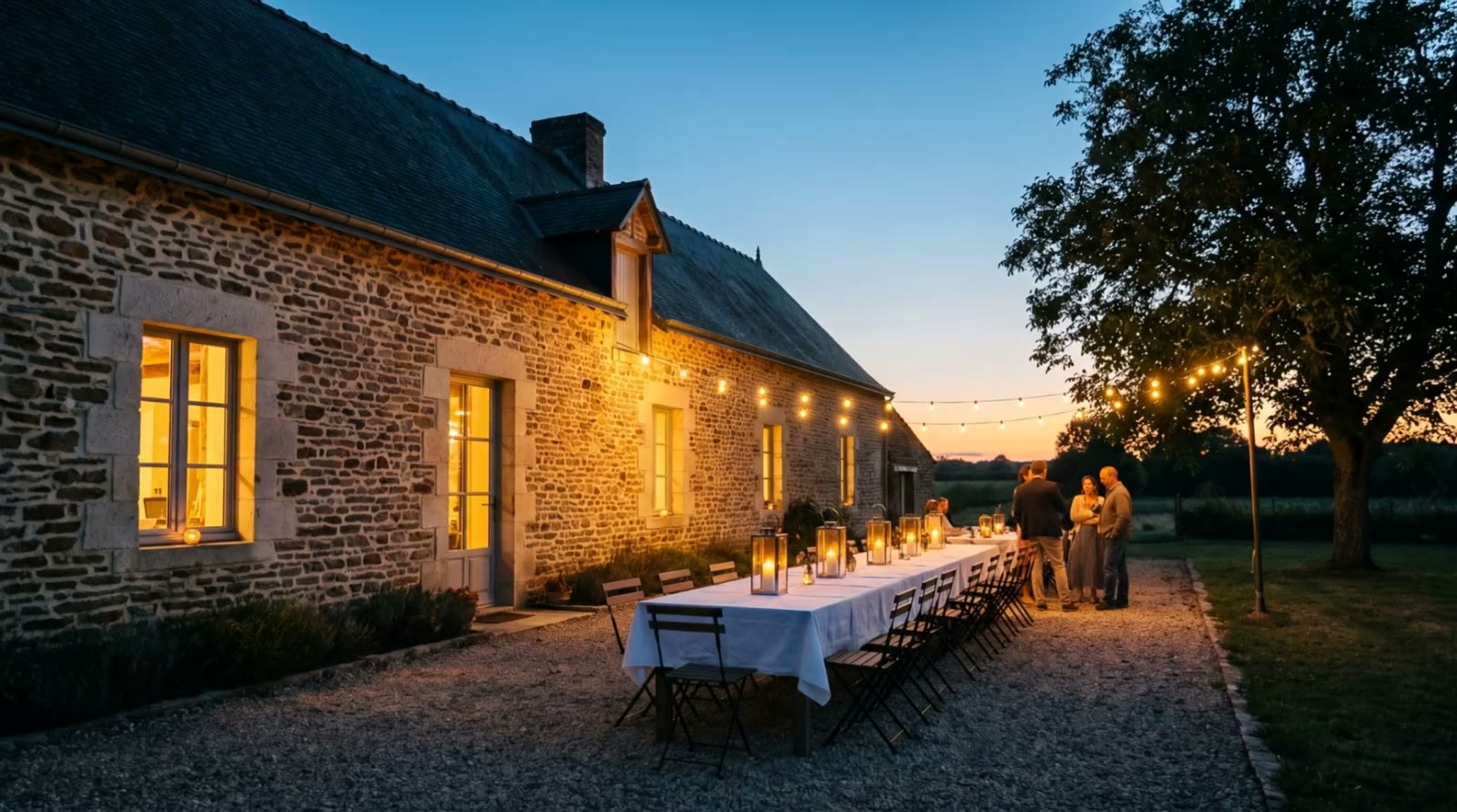 Une longère aux fenêtres allumées à l'heure bleue, une grande table dressée dehors